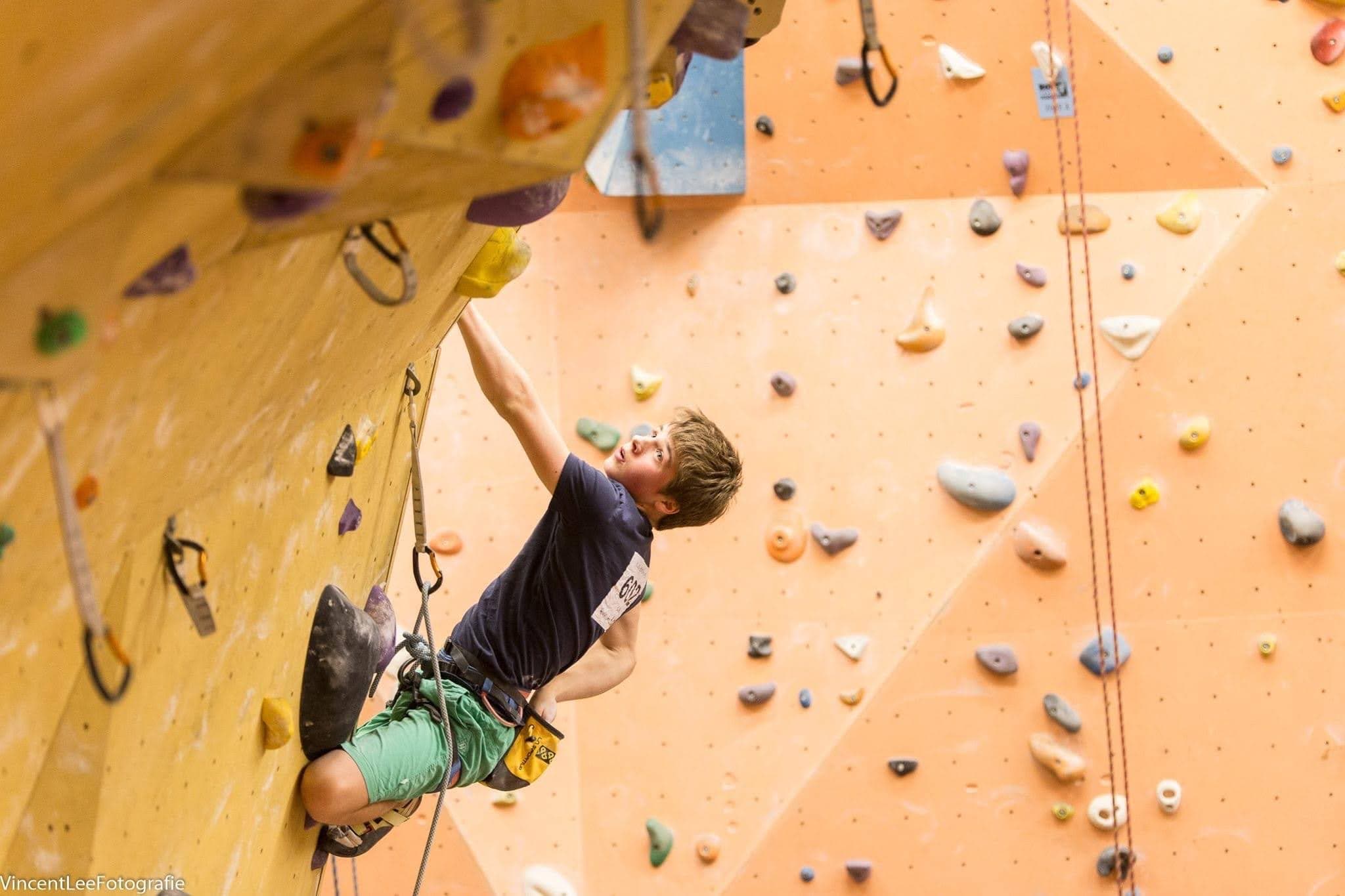 Reaching for a hold high on an orange competition wall