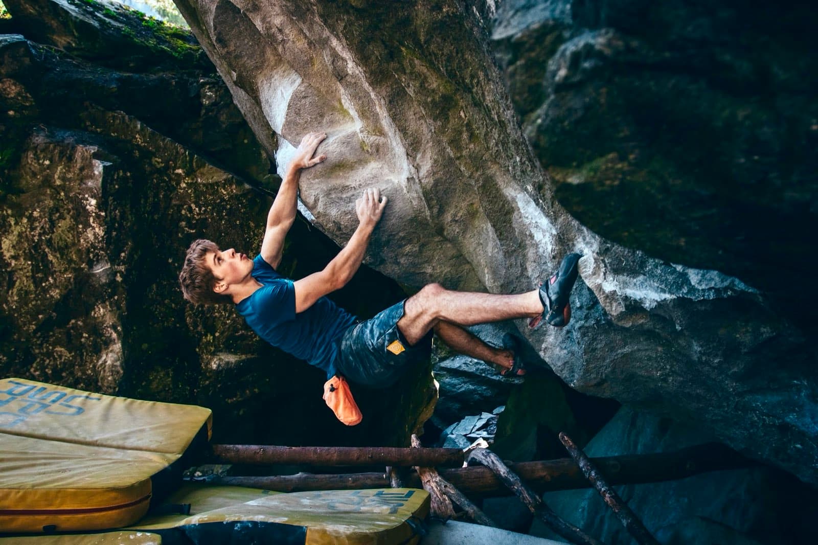Bouldering a steep grey boulder outdoors with crash pads laid out below