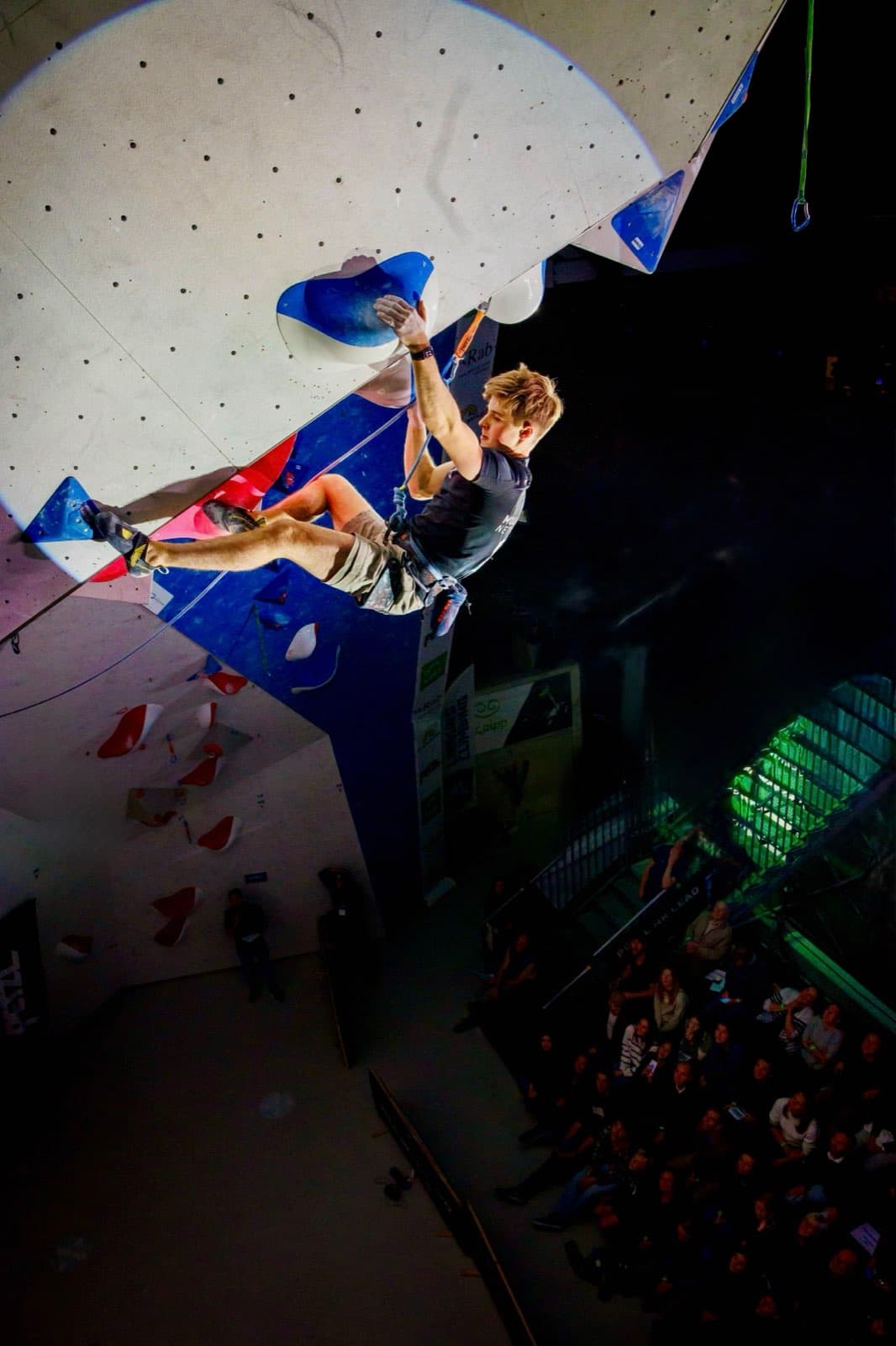 High on a floodlit blue and white competition wall above a seated audience