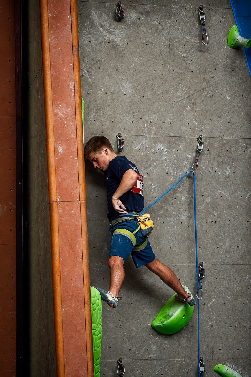Resting with the head against the wall mid-route on a competition lead climb, bib visible