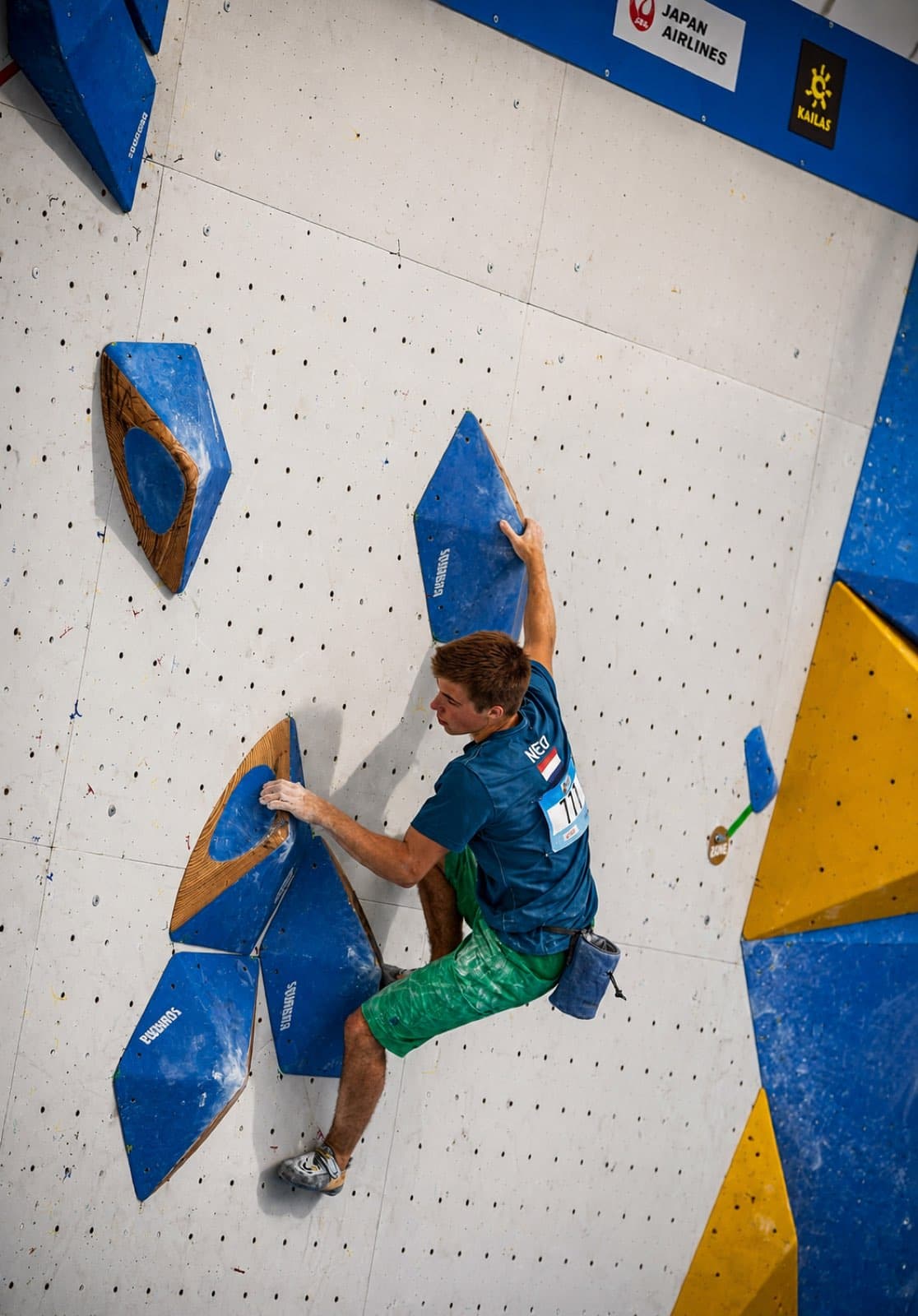 Climbing between blue wooden-framed volumes on a white competition wall