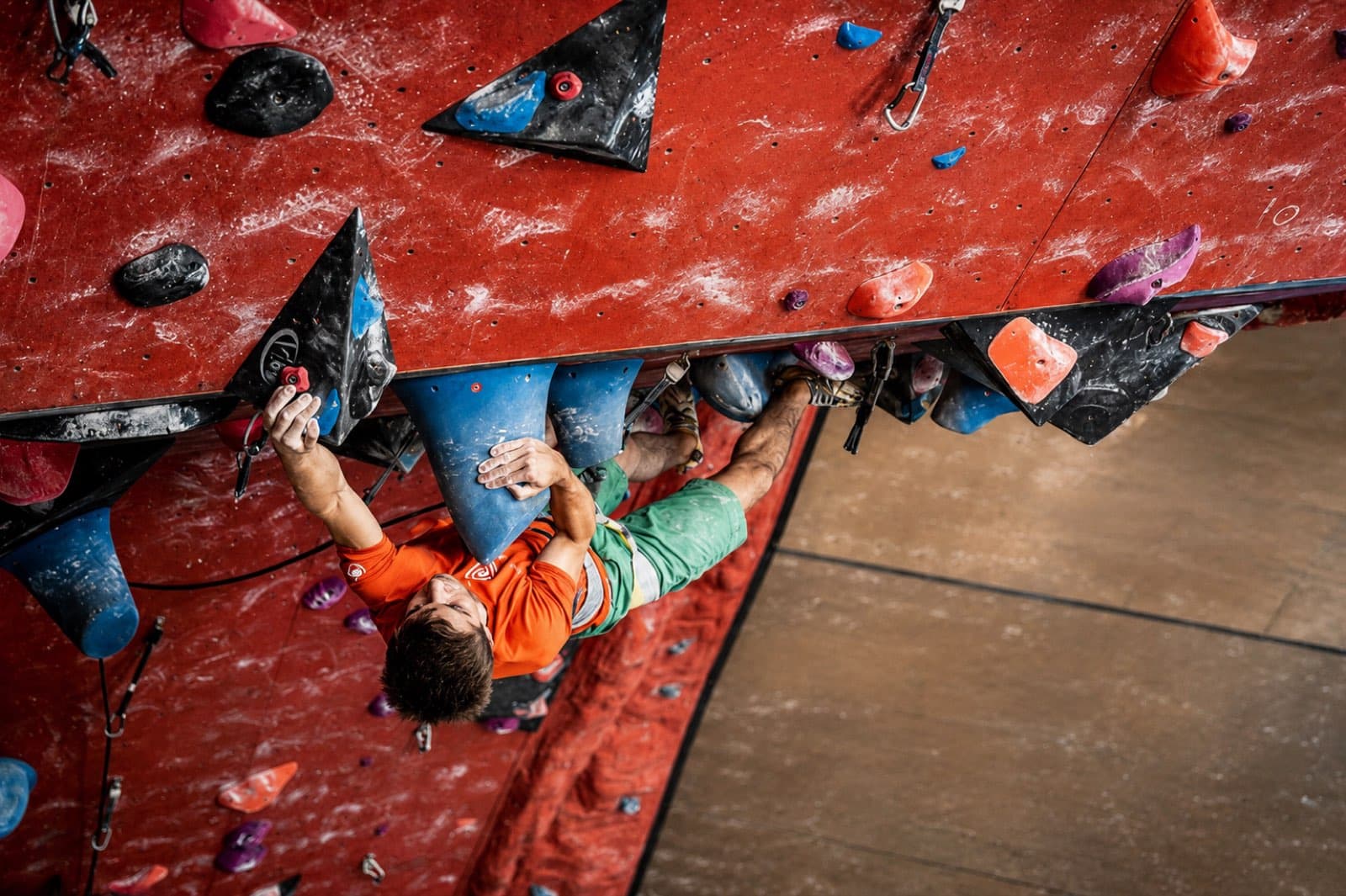 Bouldering out under a steep red indoor roof, seen from above