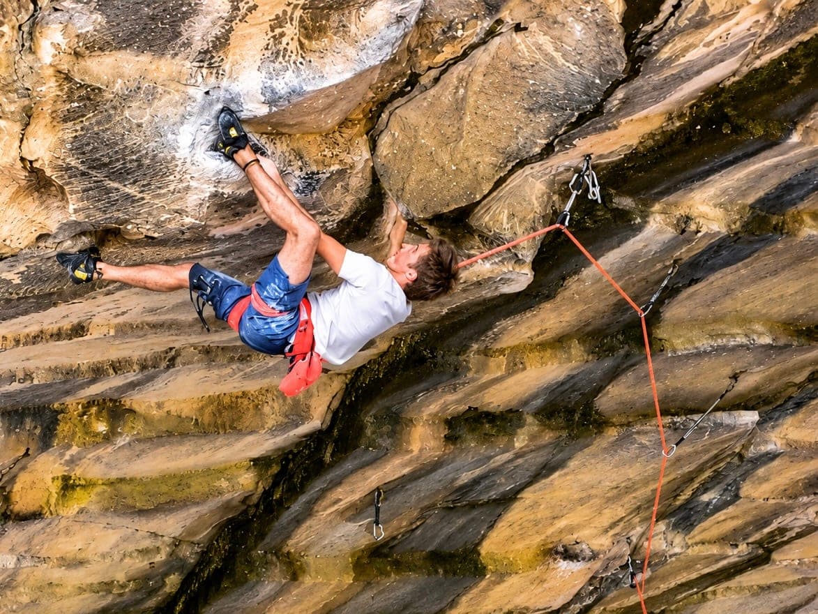 Heel-hooking through the horizontal roof of the cave on Underground, the rope running out to the right