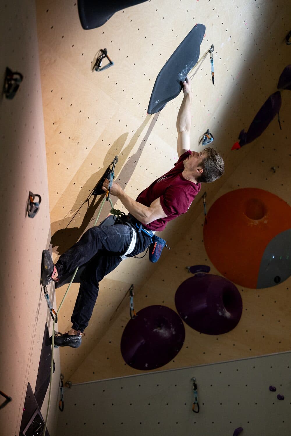 Lead climbing at the Dutch National Lead Championship 2026, reaching for a black volume on an overhanging indoor wall