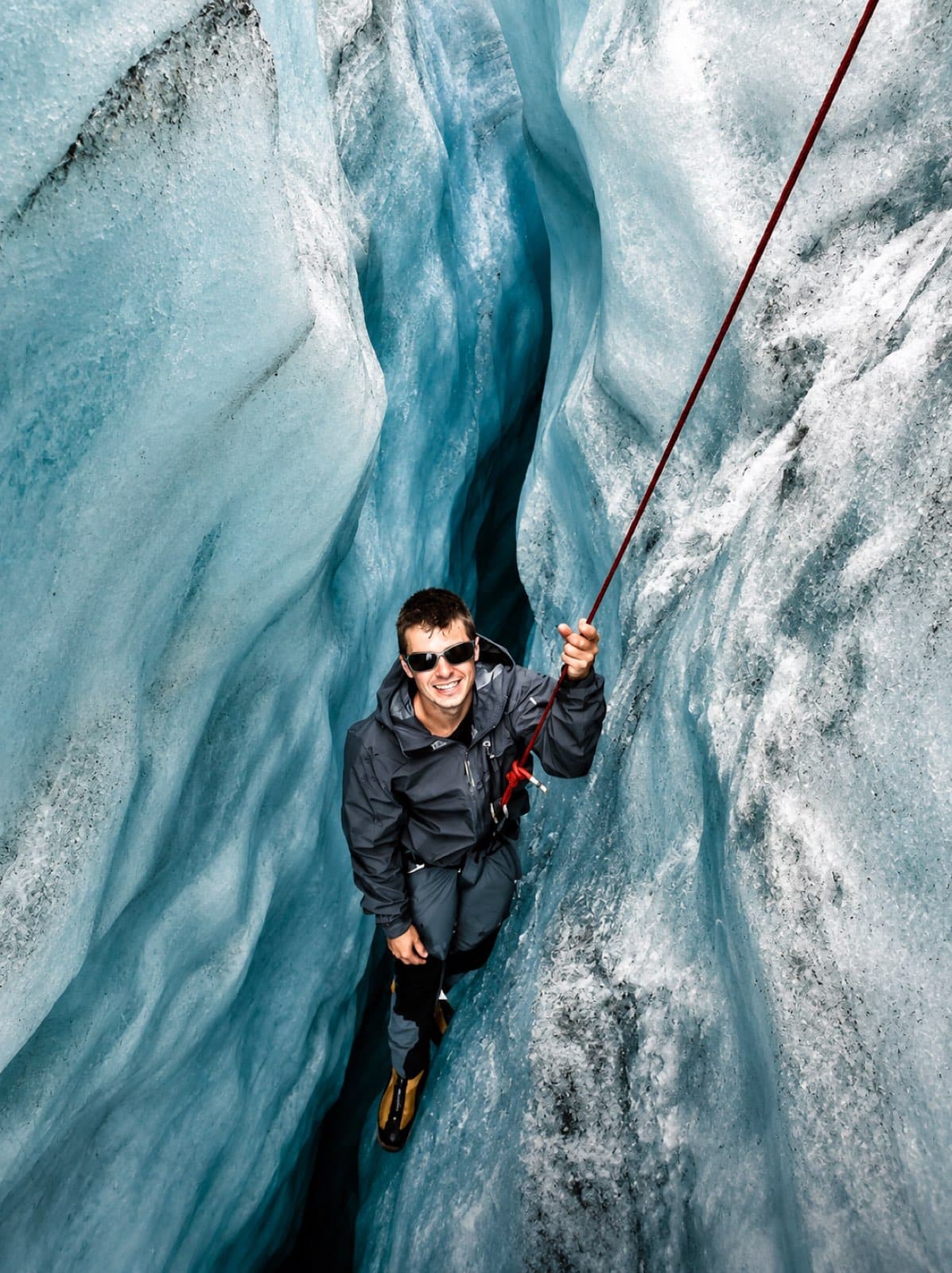 Practising crevasse rescue on a rope inside a narrow blue crevasse during alpine training, seen from above