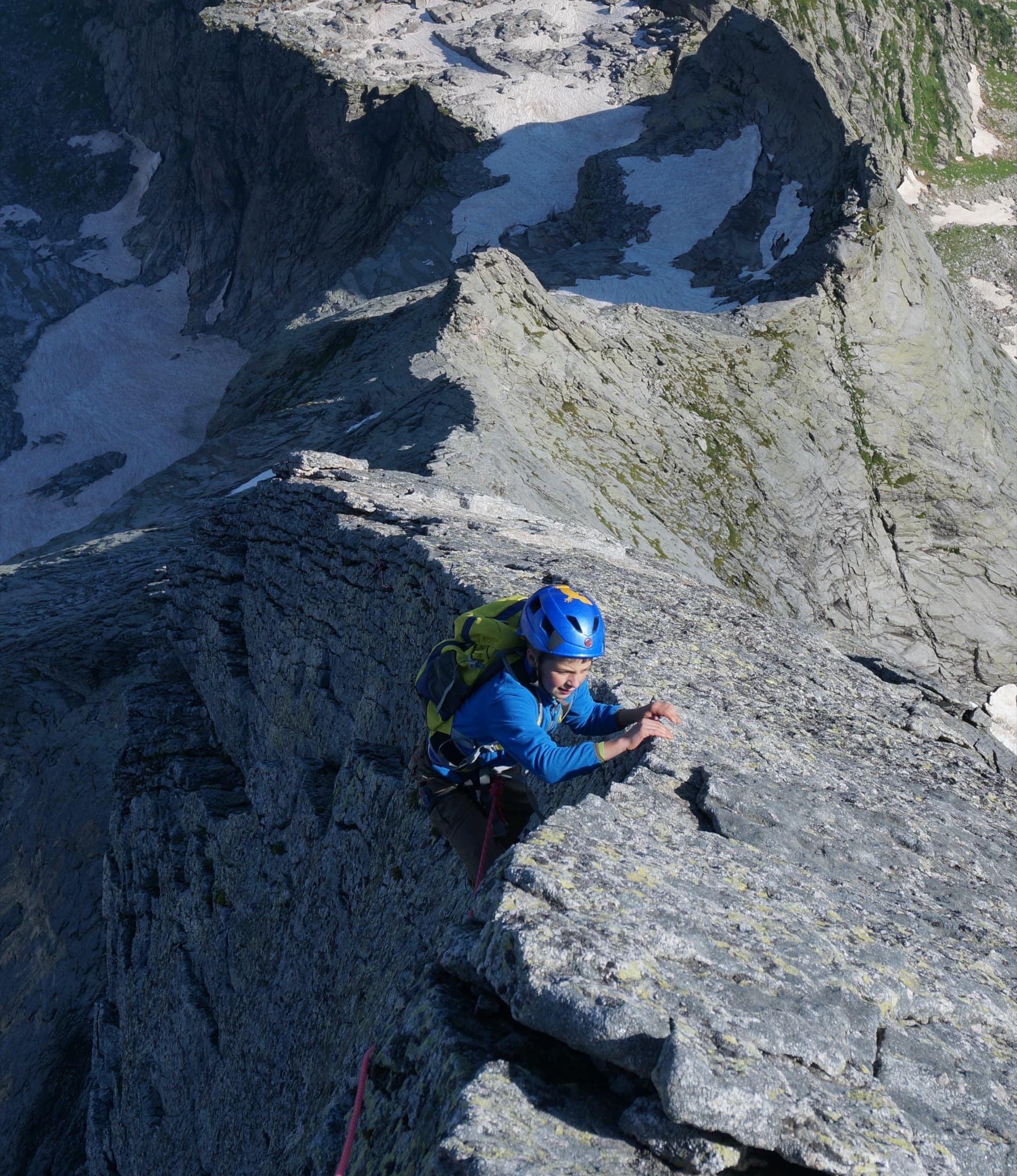 A young climber on the granite north ridge of Piz Badile, wearing a helmet and pack
