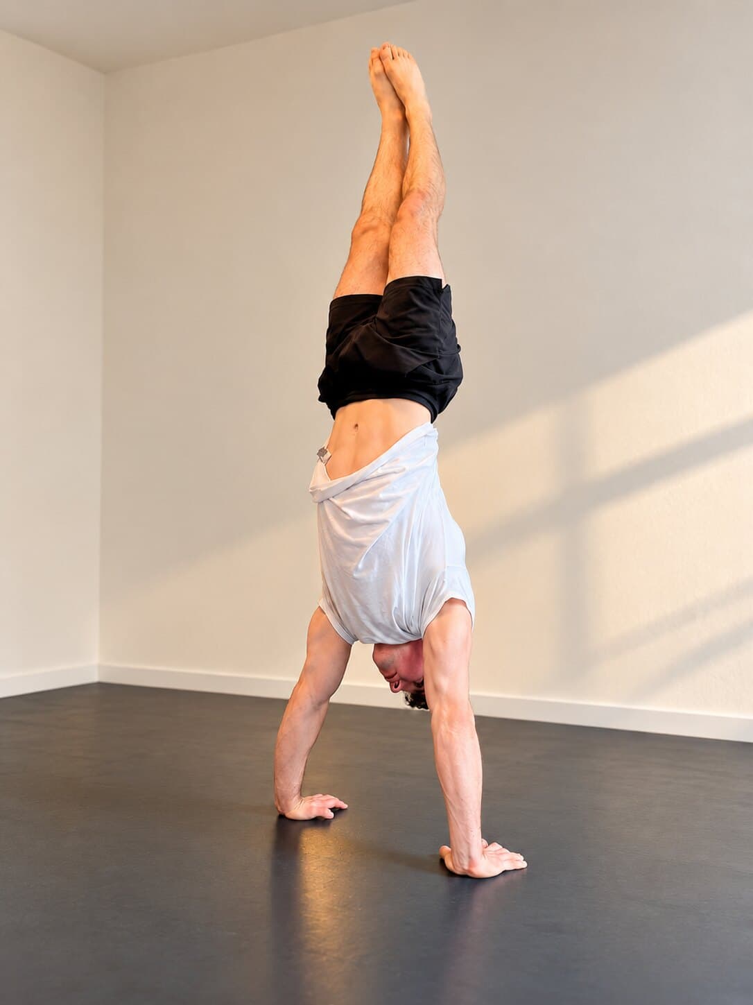 Holding a straight handstand in a studio, legs together overhead, feet pointed