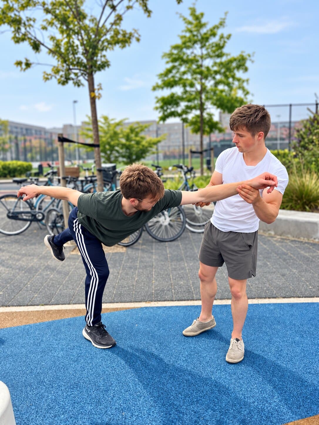 Outdoors, one practitioner grips the other's extended arm with both hands and pulls him off balance, leaving him tipped forward on one leg with the other lifted behind