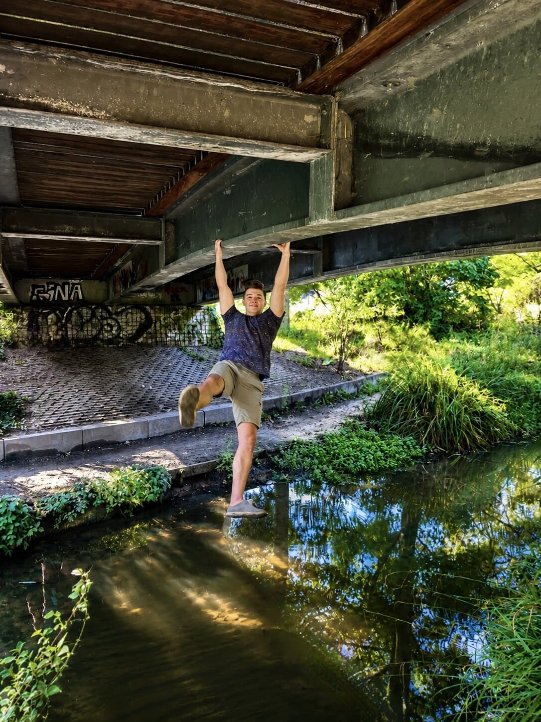 Swinging from the underside of a bridge above a canal, one leg extended over the water