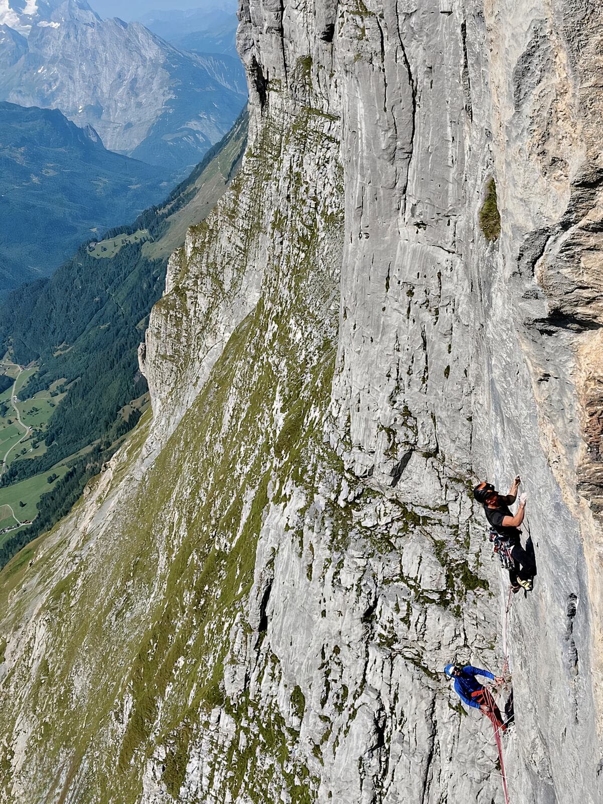 Two climbers on the steep grey limestone of the Wendenstöcke, the valley and far peaks dropping away to the left